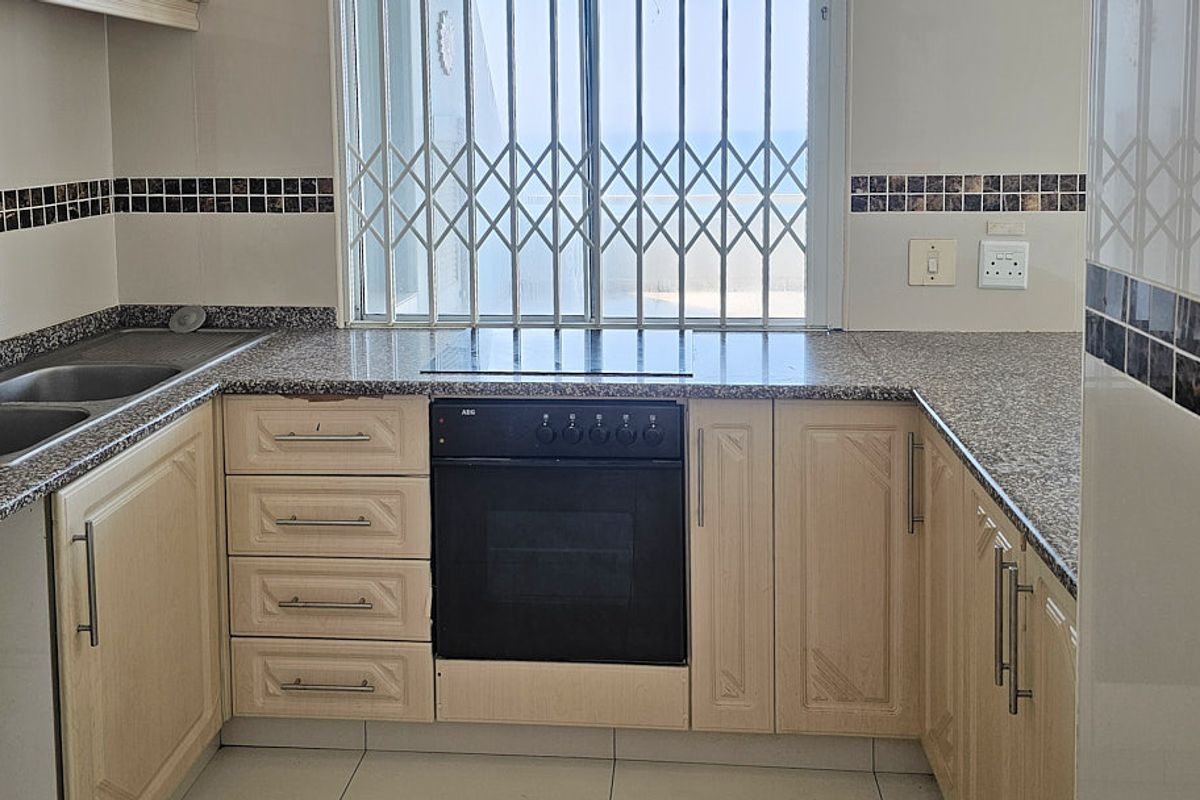 A functional kitchen featuring granite countertops, built-in oven, electric hob, and double basin sink, with a window overlooking the exterior.