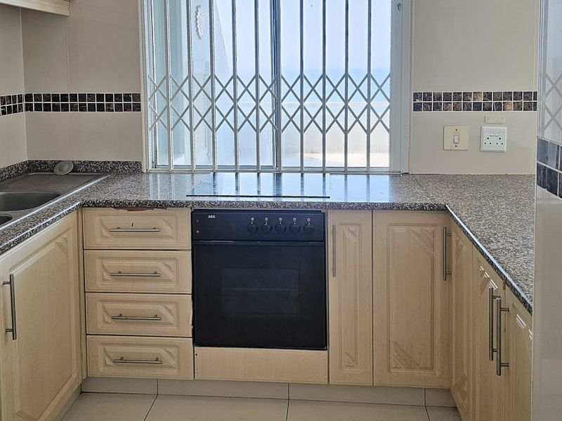 A functional kitchen featuring granite countertops, built-in oven, electric hob, and double basin sink, with a window overlooking the exterior.