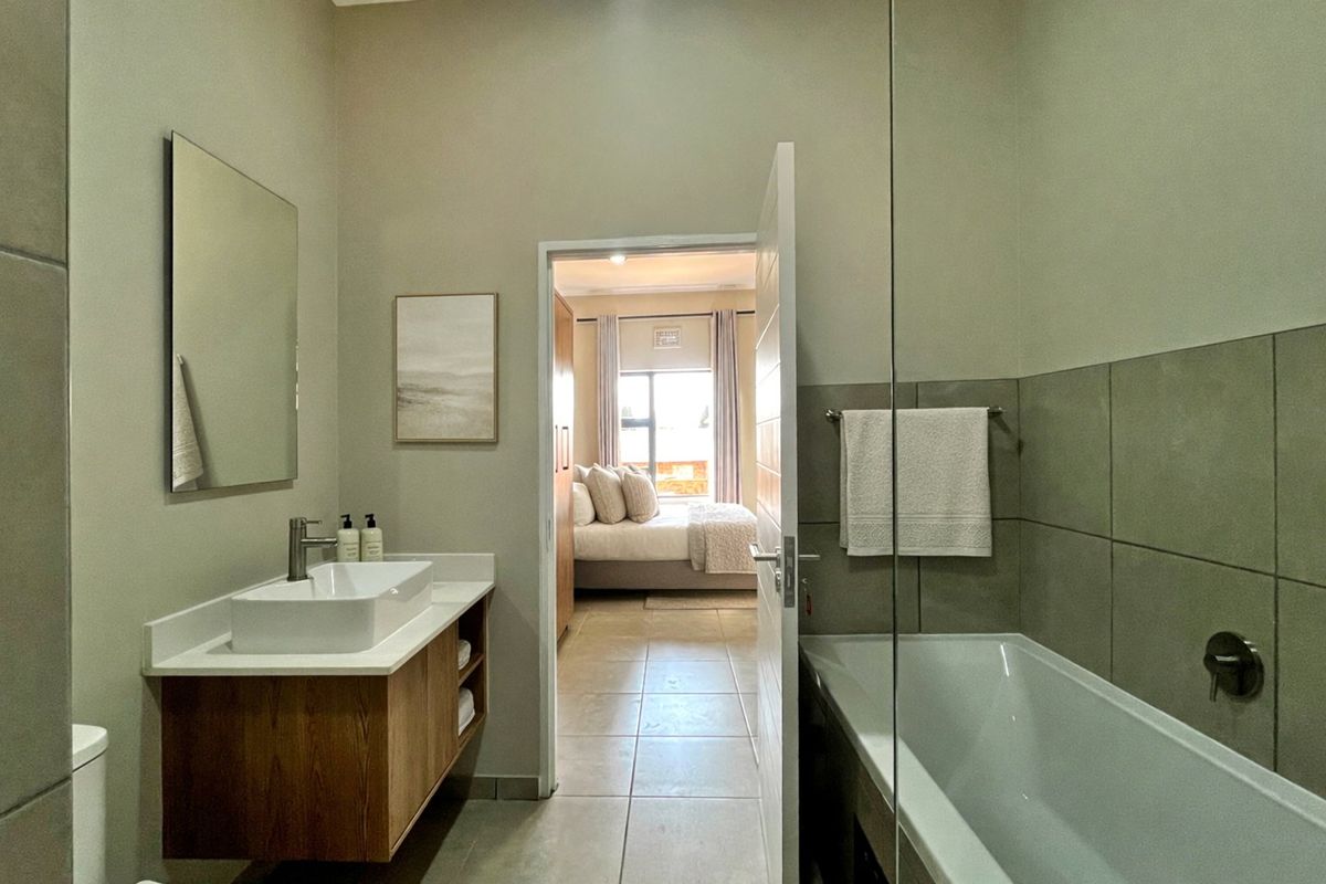 Modern bathroom featuring a floating vanity with a vessel sink, a built-in bathtub with a glass screen, and neutral floor-to-ceiling tiling.