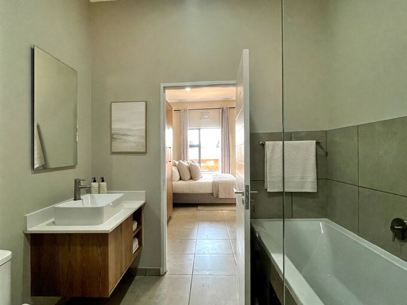 Modern bathroom featuring a floating vanity with a vessel sink, a built-in bathtub with a glass screen, and neutral floor-to-ceiling tiling.