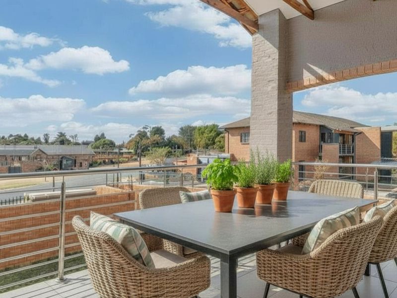 A spacious covered balcony featuring tiled flooring, a stainless steel balustrade, and exposed timber rafters, offering an elevated view of the surrounding neighbourhood.