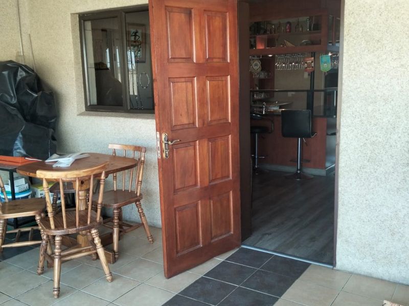 A covered patio area featuring tiled flooring and a timber entrance door leading into an interior bar space.