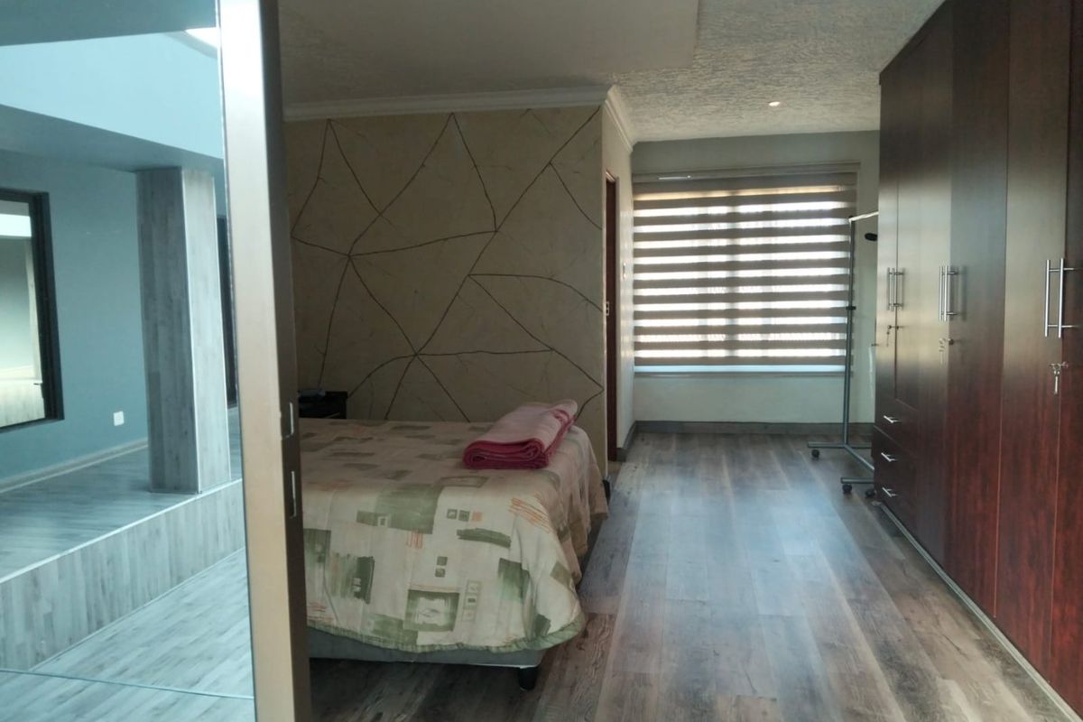 Spacious bedroom featuring modern laminate flooring, extensive built-in dark wood cabinetry, and a decorative feature wall with integrated lighting.