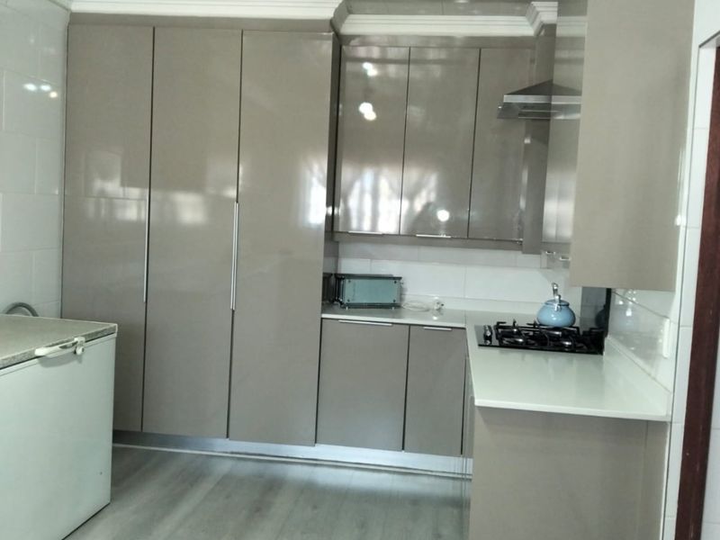 Modern kitchen featuring high-gloss cabinetry, a gas hob with extractor fan, tiled backsplash, and durable laminate flooring.