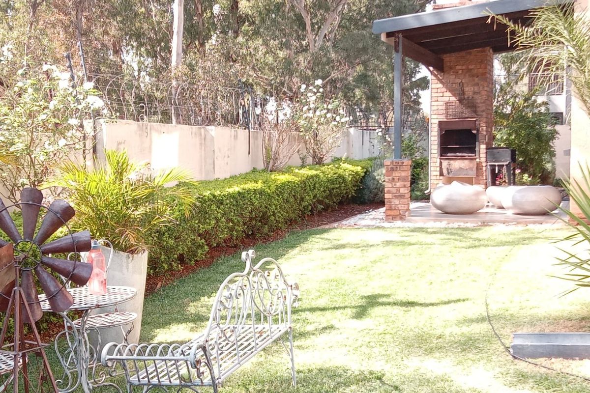 A private garden area featuring a covered patio with a built-in brick braai, surrounded by a perimeter wall with security fencing.