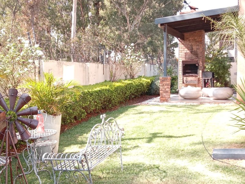 A private garden area featuring a covered patio with a built-in brick braai, surrounded by a perimeter wall with security fencing.