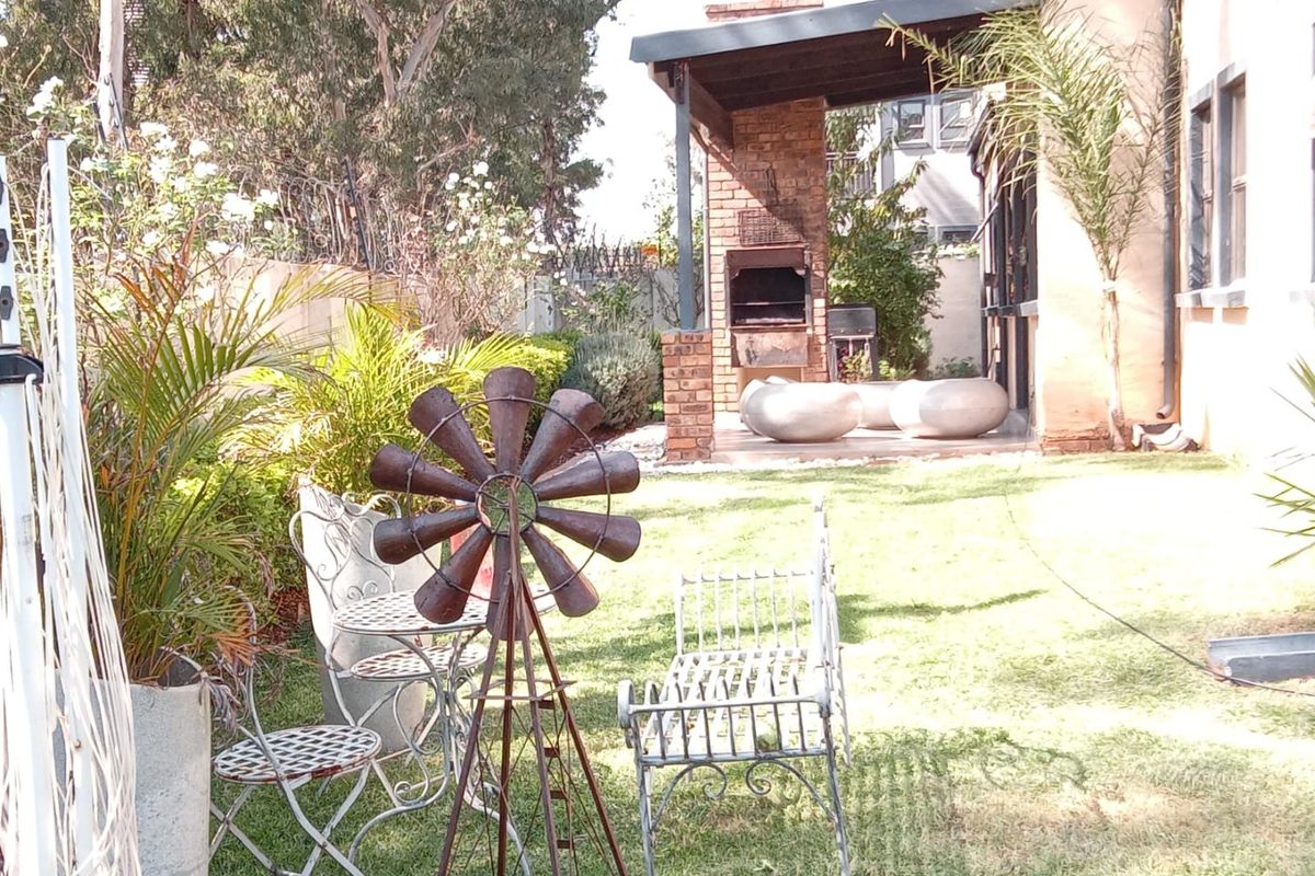 A rear garden area featuring a built-in brick braai under a covered patio, overlooking a lawn and established perimeter landscaping.