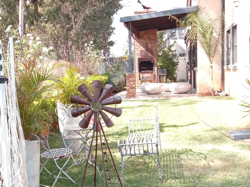 A rear garden area featuring a built-in brick braai under a covered patio, overlooking a lawn and established perimeter landscaping.