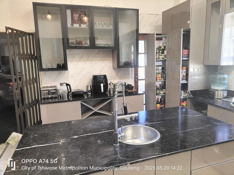 Modern kitchen featuring dark marble-look countertops, sleek cabinetry, a pull-out pantry, and a central island with a stainless steel sink and gooseneck faucet.