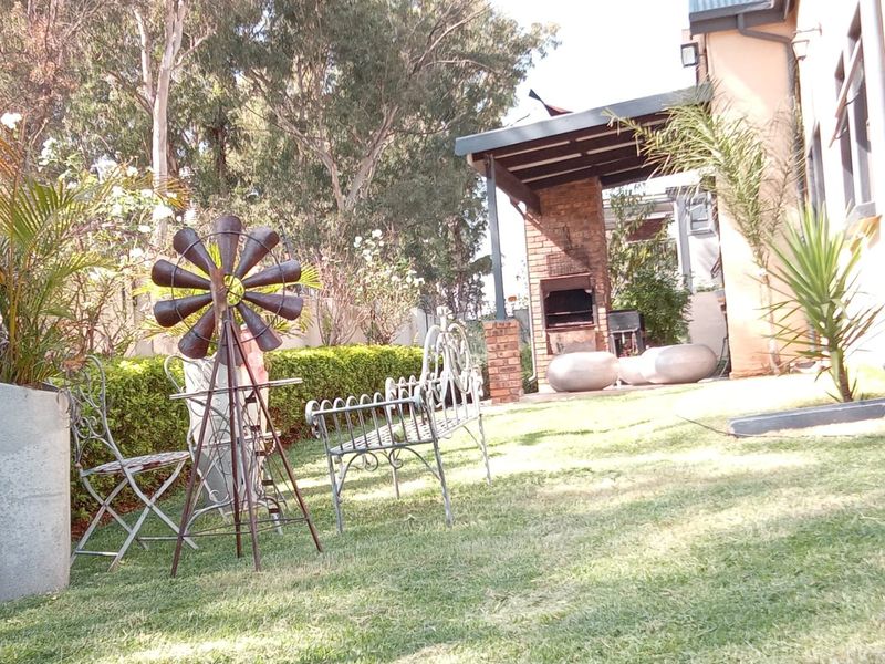 A backyard area featuring a covered patio with a built-in brick braai, overlooking a landscaped garden with established trees and hedging.