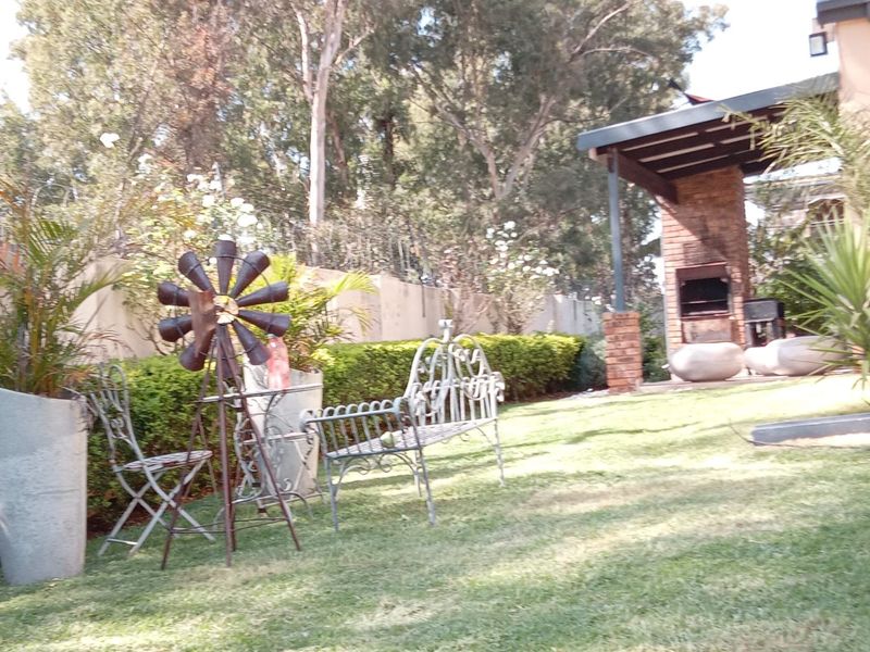 A rear garden area featuring a built-in brick braai and a covered patio space, set against a backdrop of mature trees and boundary walls.