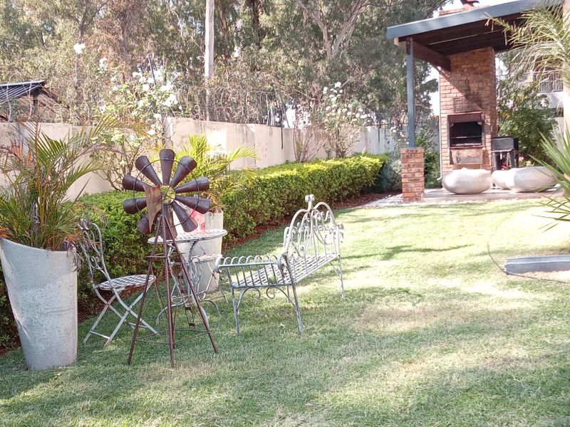 A private rear garden featuring a well-maintained lawn, established hedges, and a covered patio area with a built-in brick braai.