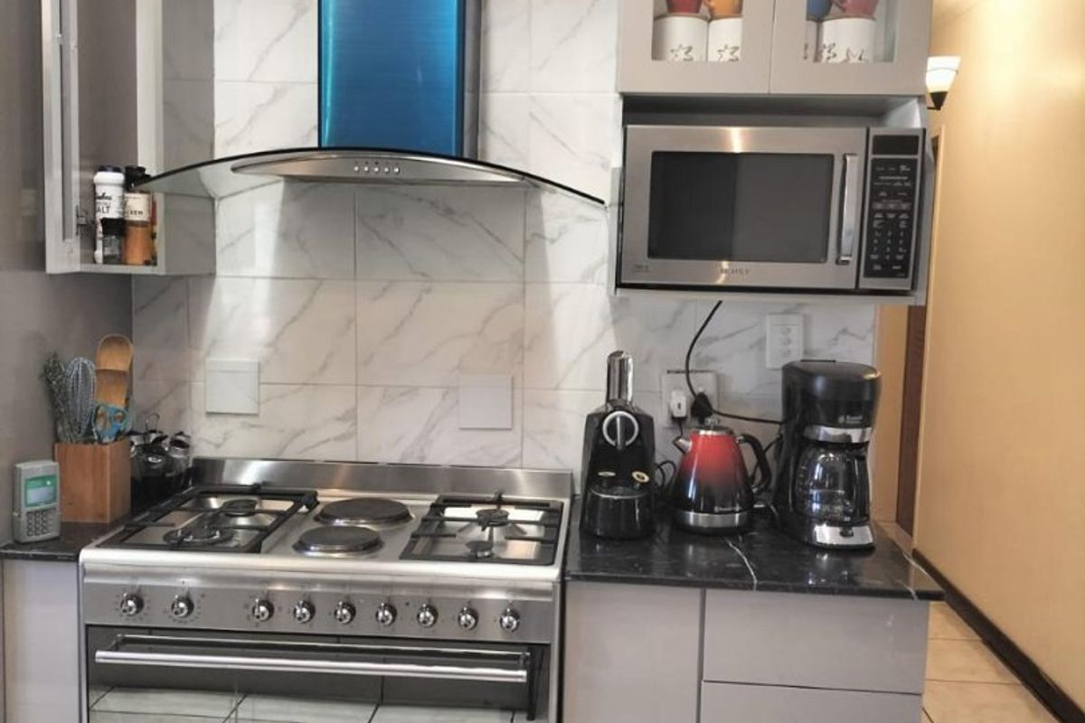 A compact, modern kitchen featuring a stainless steel gas stove, extractor fan, built-in microwave, granite countertops, and elegant marble-look tile backsplash.