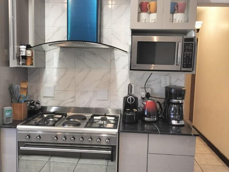 A compact, modern kitchen featuring a stainless steel gas stove, extractor fan, built-in microwave, granite countertops, and elegant marble-look tile backsplash.