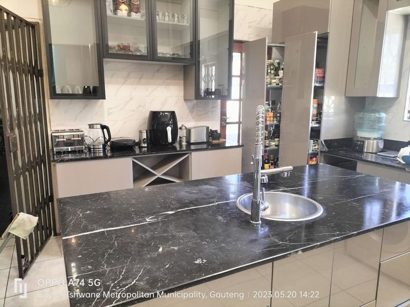 Modern kitchen featuring a central island with a dark marble-look countertop, gooseneck faucet, and ample built-in cabinetry with glass-front upper units.