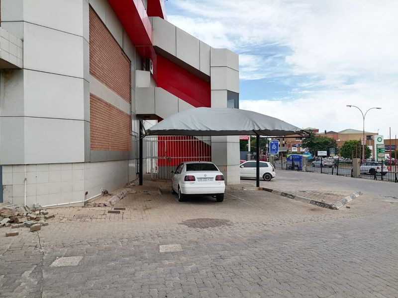 Rear exterior view of the commercial property featuring a covered parking bay, paved driveway, and metal security gate access.