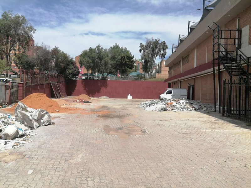 Rear exterior area of a commercial property featuring paved ground, a brick retaining wall, and an external metal staircase, currently cluttered with construction debris.