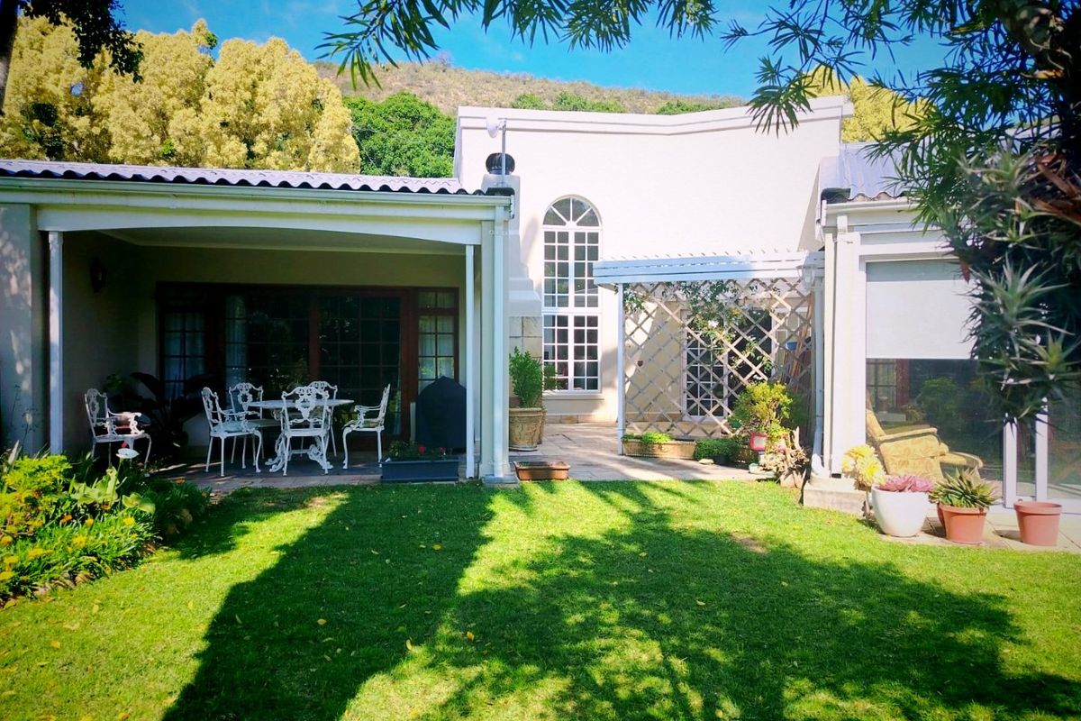 A well-maintained rear exterior view featuring a covered patio, paved terrace area, and a landscaped garden with a lawn.