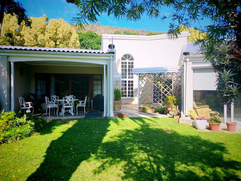 A well-maintained rear exterior view featuring a covered patio, paved terrace area, and a landscaped garden with a lawn.