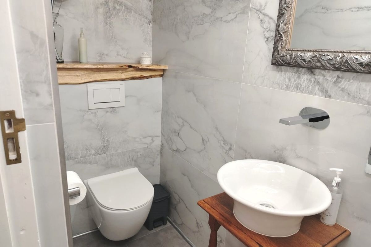 Modern bathroom featuring marble-effect wall tiles, a wall-mounted toilet with concealed cistern, and a stylish vessel sink with wall-mounted faucet.
