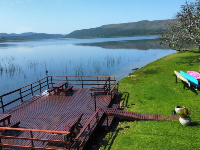 A scenic timber deck extending over the water, featuring a wooden railing and direct access to a well-maintained lawn and lakefront.
