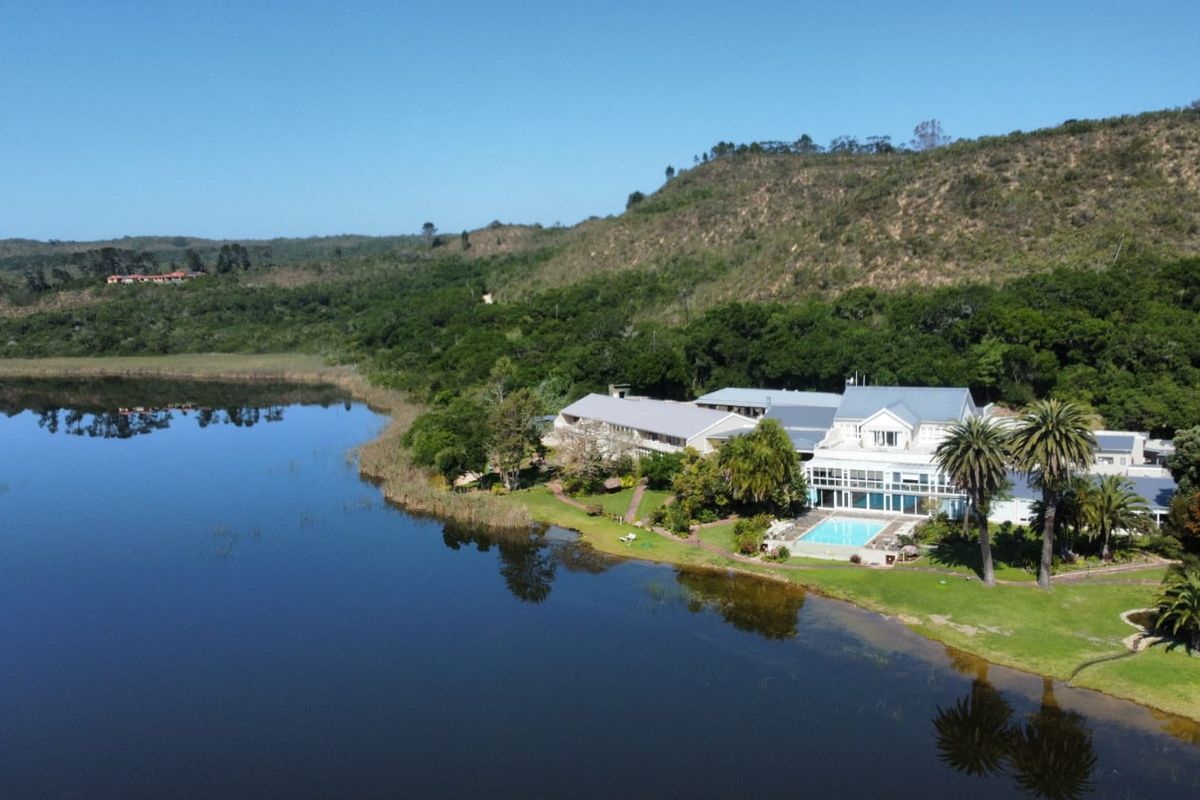 Aerial view of a large property situated on a lakefront, featuring a swimming pool, expansive lawns, and mature trees.