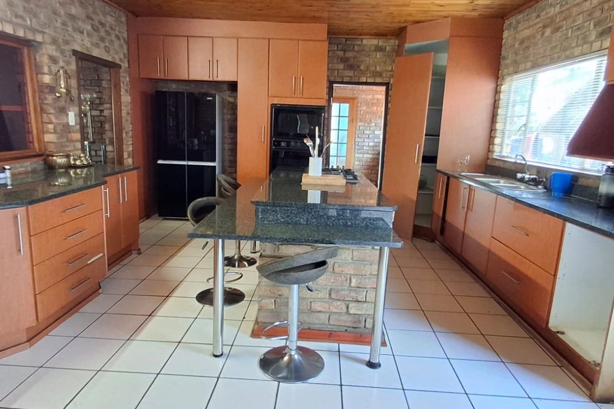 Spacious kitchen featuring granite countertops, exposed brick walls, timber ceiling, and ample cabinetry, offering a functional layout with a central island.