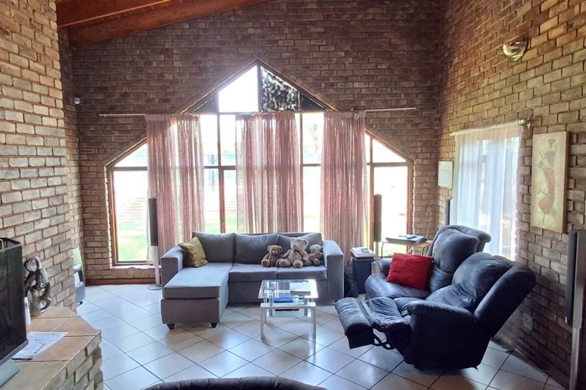 Spacious living room featuring exposed brick walls, a vaulted timber ceiling, tiled flooring, and a large feature window with natural light.