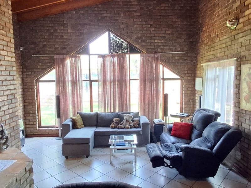 Spacious living room featuring exposed brick walls, a vaulted timber ceiling, tiled flooring, and a large feature window with natural light.