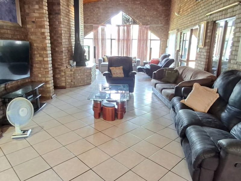 Spacious living room featuring exposed brick walls, vaulted ceilings, tiled flooring, and a central fireplace, offering a rustic and open atmosphere.
