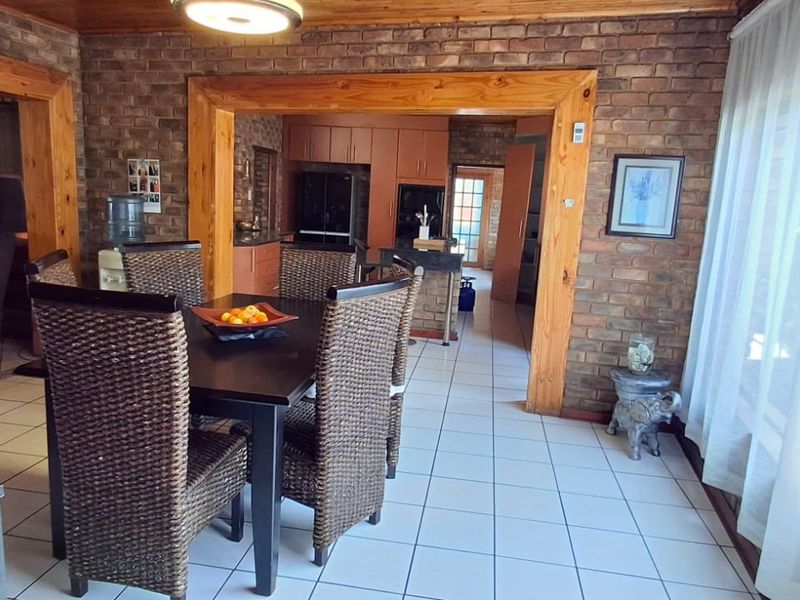 Open plan dining and kitchen area featuring exposed brick walls, timber accents, and ceramic tiled flooring with a view into the adjacent kitchen.