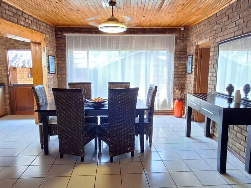 Open-plan dining area featuring exposed brick walls, timber ceiling, and ceramic floor tiles, with an adjacent kitchen visible in the background.