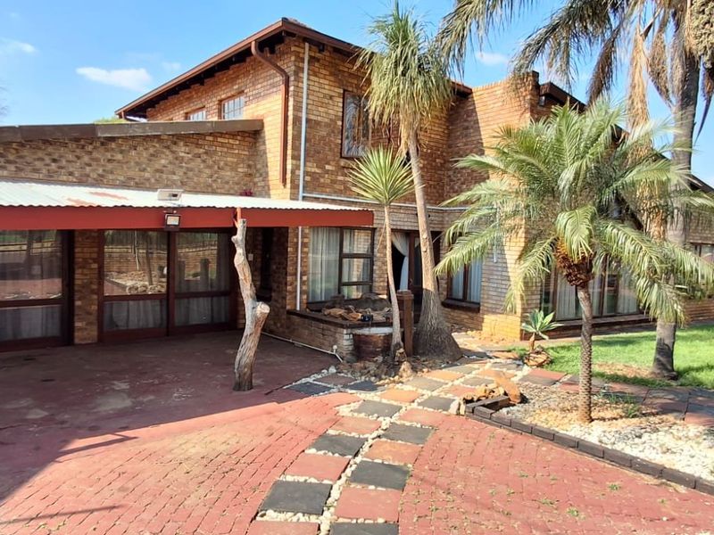 Rear view of a double-story brick house featuring a covered patio area, paved driveway, and established garden.