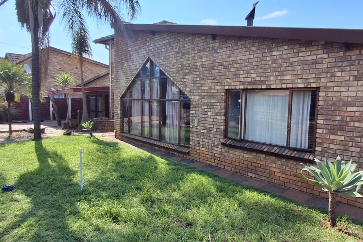 Rear view of a face brick house featuring a distinctive triangular window, pitched roofline, and established garden area.