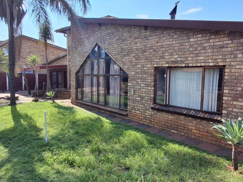 Rear view of a face brick house featuring a distinctive triangular window, pitched roofline, and established garden area.