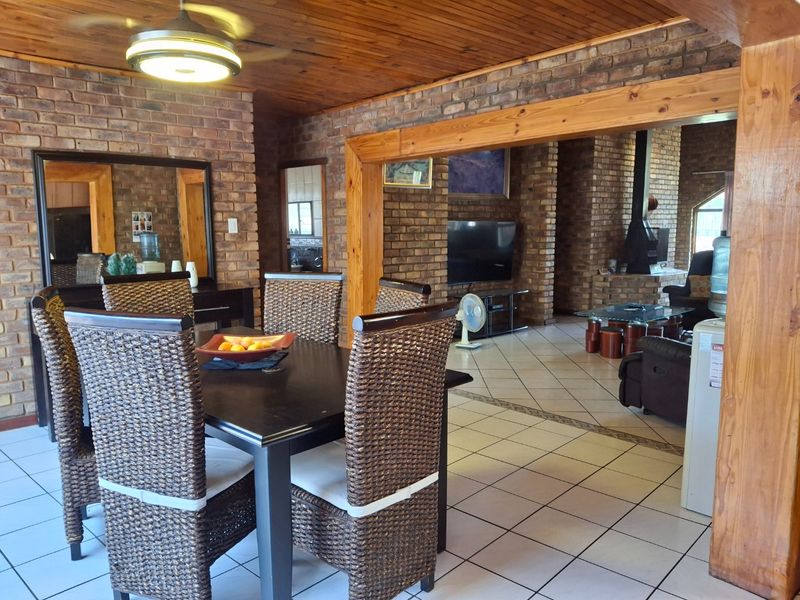 Spacious open-plan living and dining area featuring exposed brick walls, timber ceiling, ceramic tiled flooring, and a built-in fireplace.