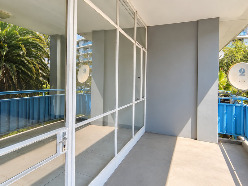 A spacious, covered balcony featuring tiled flooring, a blue metal balustrade, and large glass sliding doors providing access to the interior.