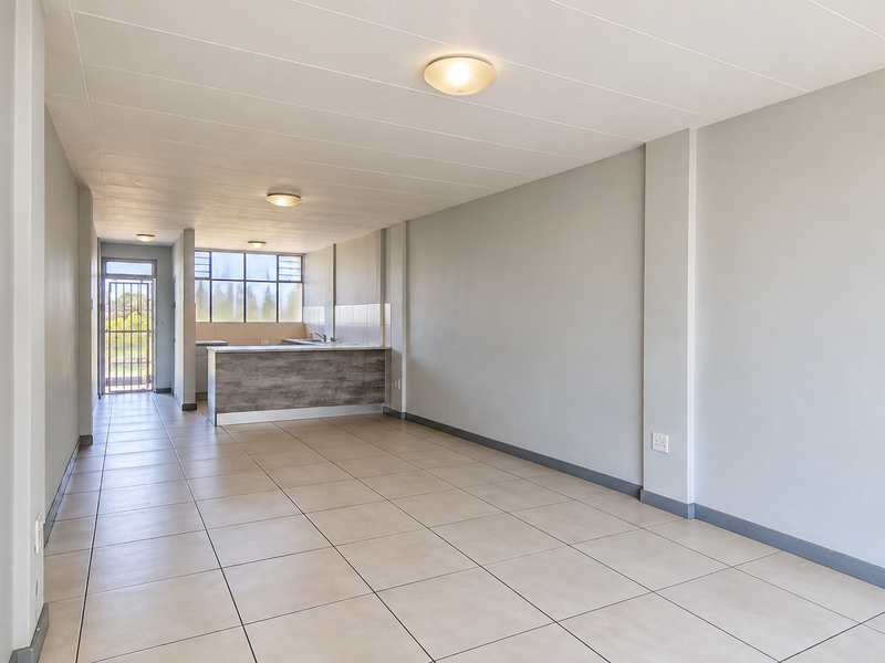 An open-plan living and kitchen area featuring neutral tiled flooring, a breakfast counter, and direct access to an exterior security gate.