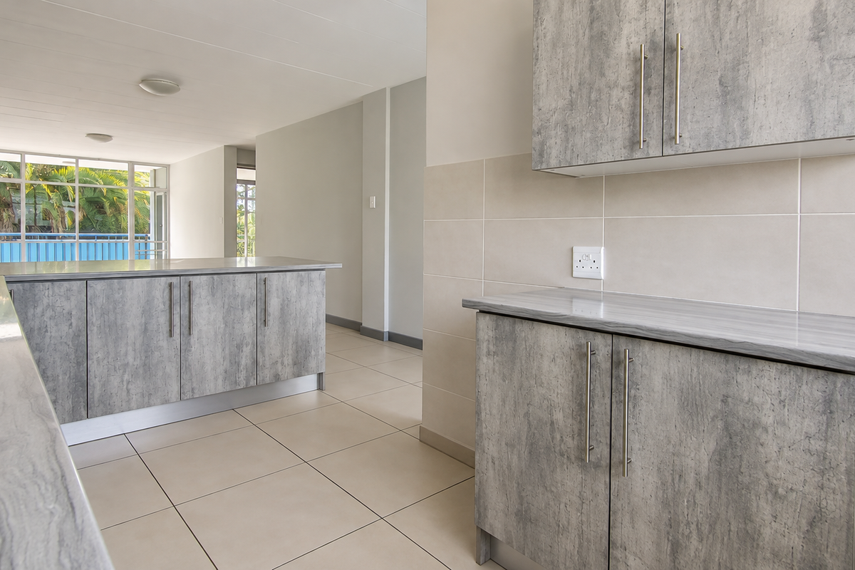 Modern kitchen featuring grey laminate cabinetry, stone-look countertops, stainless steel sink, and neutral ceramic tiling throughout the open-plan space.