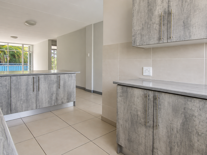 Modern kitchen featuring grey laminate cabinetry, stone-look countertops, stainless steel sink, and neutral ceramic tiling throughout the open-plan space.