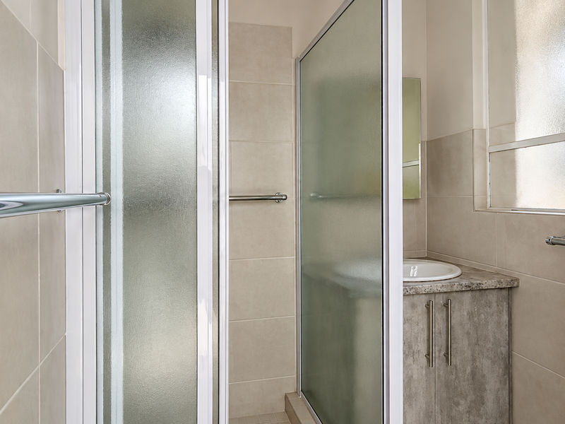 A functional bathroom featuring a shower enclosure, a vanity cabinet with a drop-in basin, and neutral wall tiling.