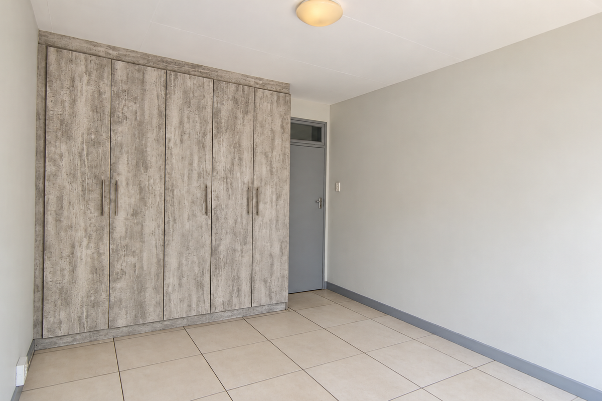 A bright, empty bedroom featuring neutral tiled flooring and extensive built-in cupboards with a modern wood-grain finish.
