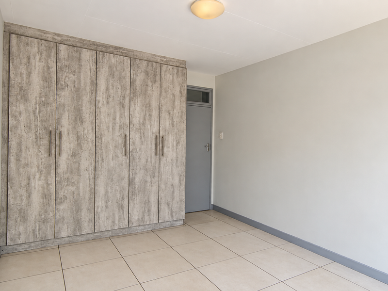 A bright, empty bedroom featuring neutral tiled flooring and extensive built-in cupboards with a modern wood-grain finish.