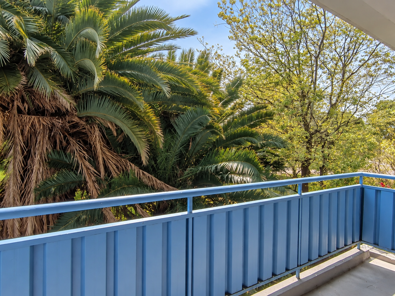 A private balcony featuring a blue metal balustrade and views of mature trees and greenery.