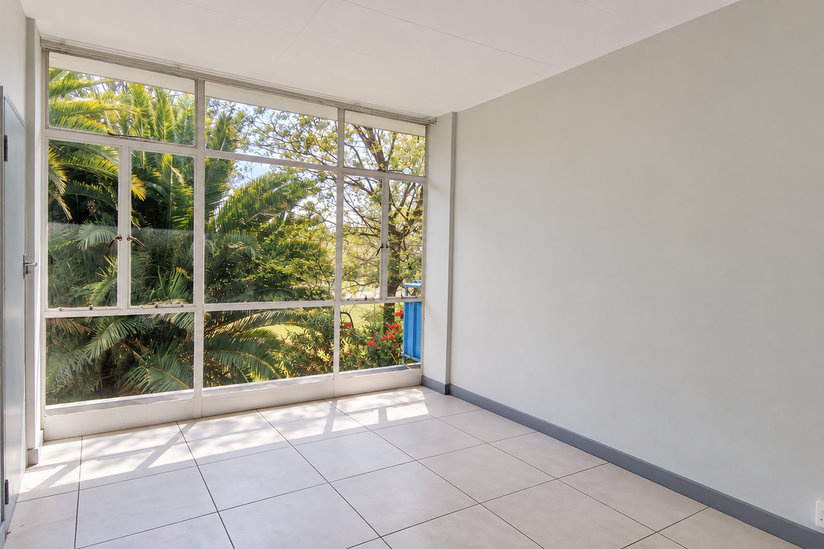 A bright, empty living area featuring large aluminium-framed windows that provide ample natural light and views of the surrounding greenery.