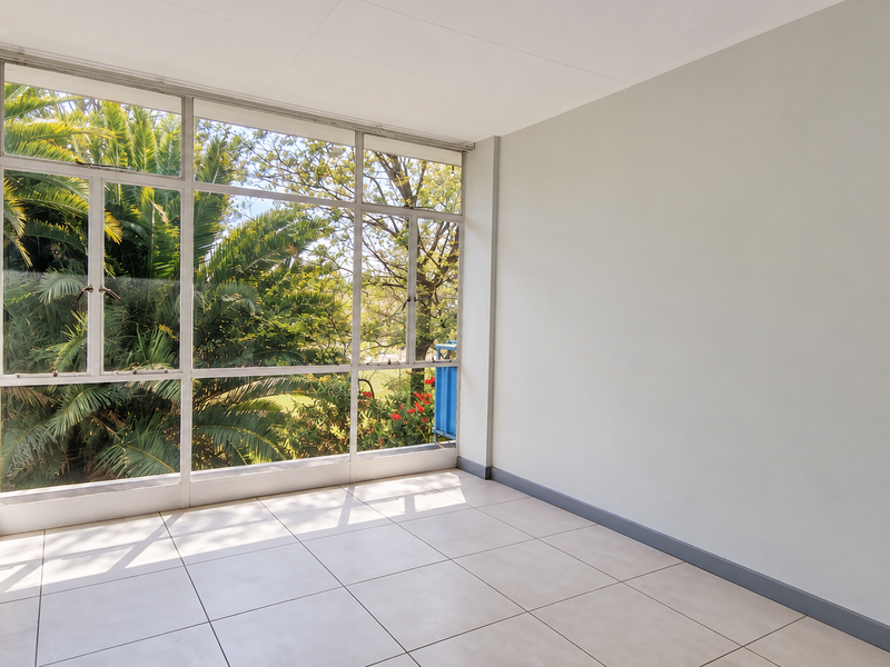 A bright, empty living area featuring large aluminium-framed windows that provide ample natural light and views of the surrounding greenery.