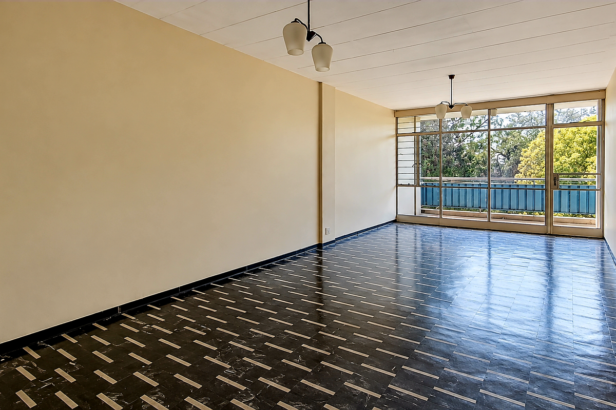 A spacious, empty living room featuring patterned tiled flooring, neutral walls, and large sliding glass doors leading to an outdoor balcony area.