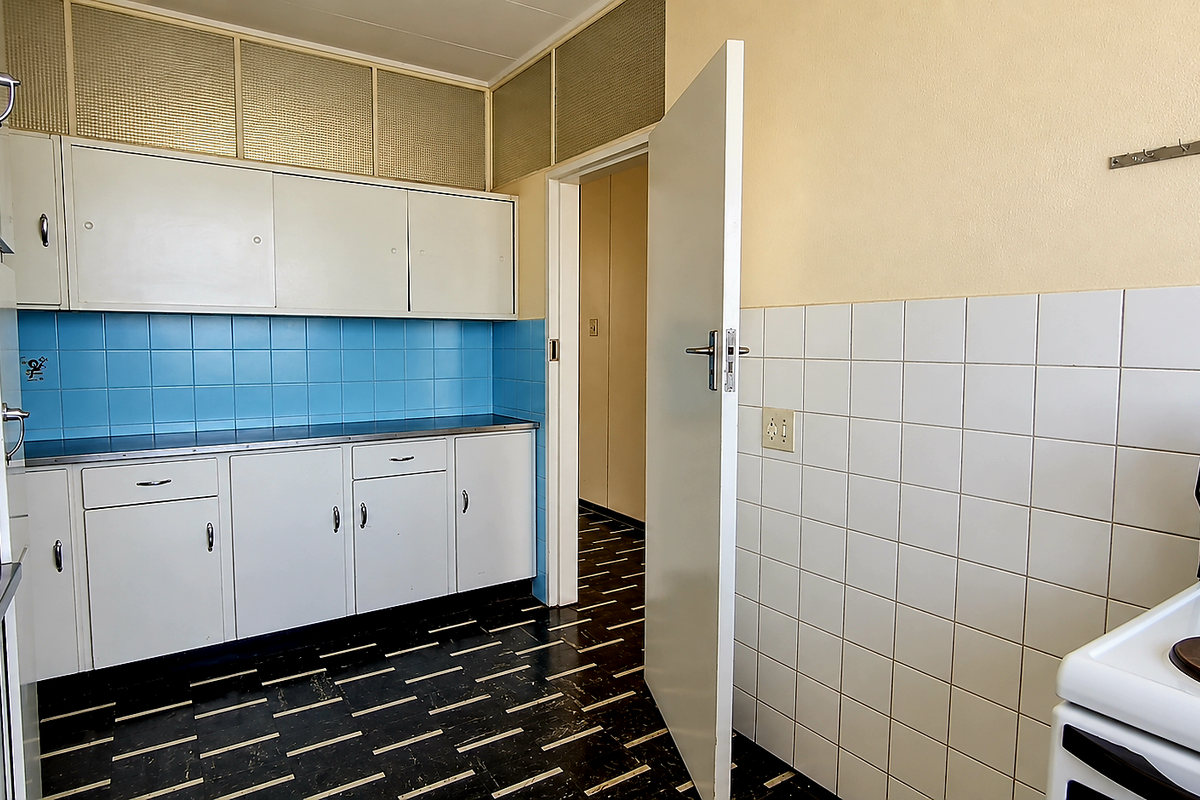 A functional, dated kitchen featuring white built-in cabinetry, blue and white tiled backsplashes, and a standalone electric stove.