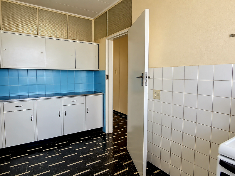 A functional, dated kitchen featuring white built-in cabinetry, blue and white tiled backsplashes, and a standalone electric stove.