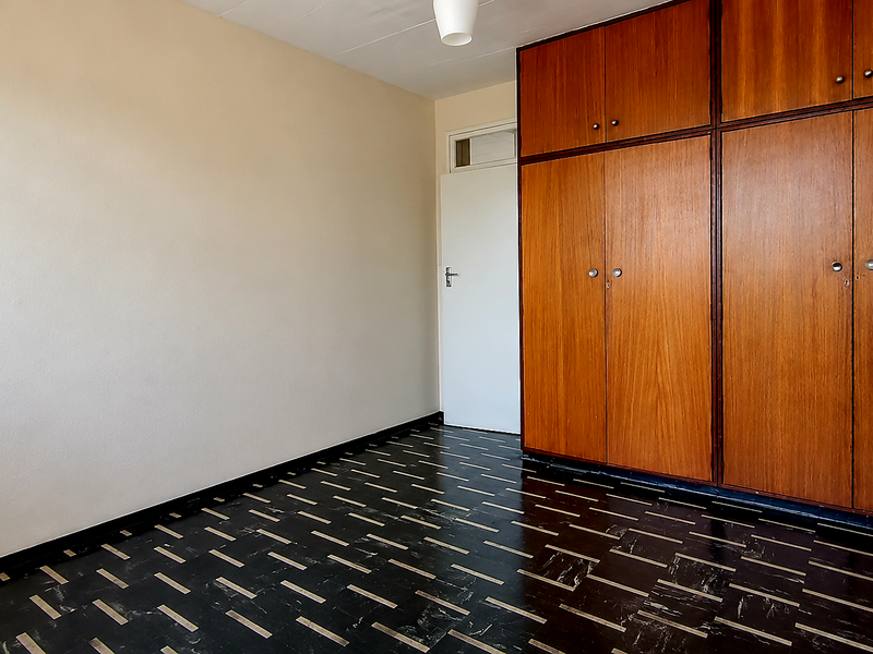 An empty bedroom featuring built-in wooden cupboards and patterned vinyl flooring, offering a blank canvas for renovation or restyling.